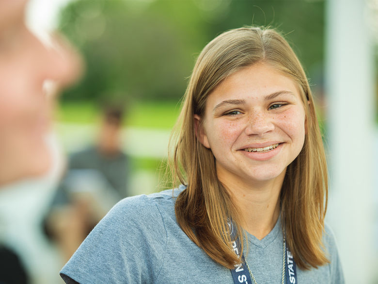 A female student wearing a Penn State lanyard smiles at another student..